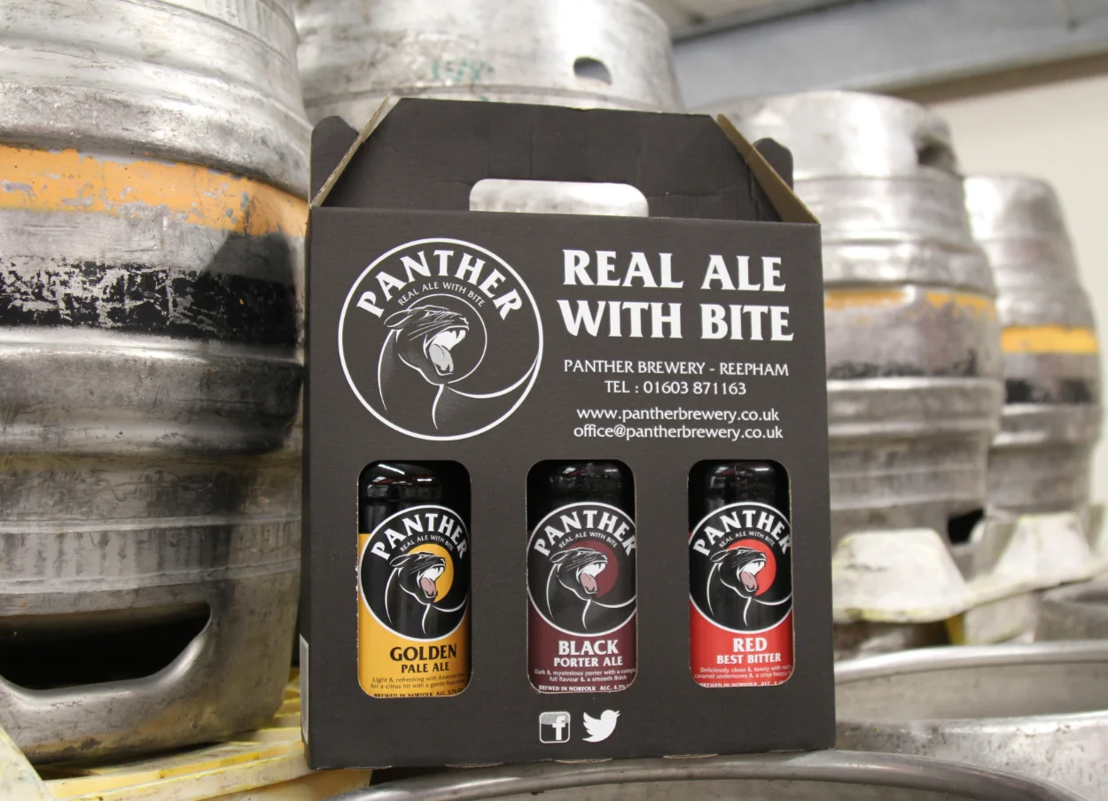 Gift pack of Panther Brewery real ales displayed in front of brewing kegs in Norfolk brewery setting